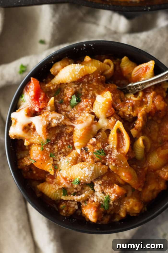 Top shot of a black bowl filled with shell pasta, red sauce, and grated parmesan.