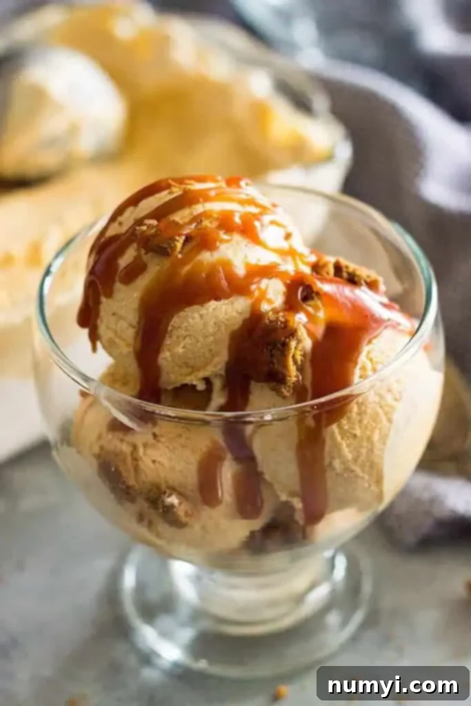 Effortless Pumpkin Ice Cream 4 A glass dish of creamy pumpkin pie ice cream, beautifully adorned with crumbled cookies and a decadent drizzle of salted caramel sauce.