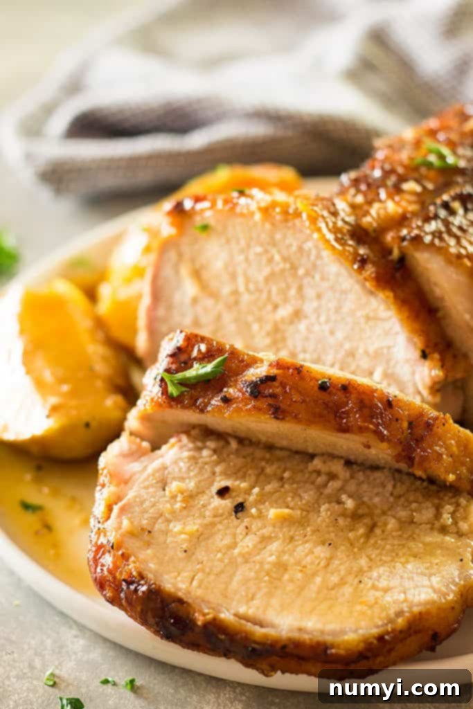 Close-up of perfectly sliced maple roasted pork loin with vibrant apples and onions on a white plate, showcasing its tenderness and rich color.