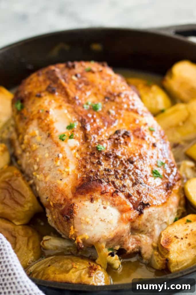 Pork loin searing in a hot skillet with a mix of apples and onions, preparing for roasting.