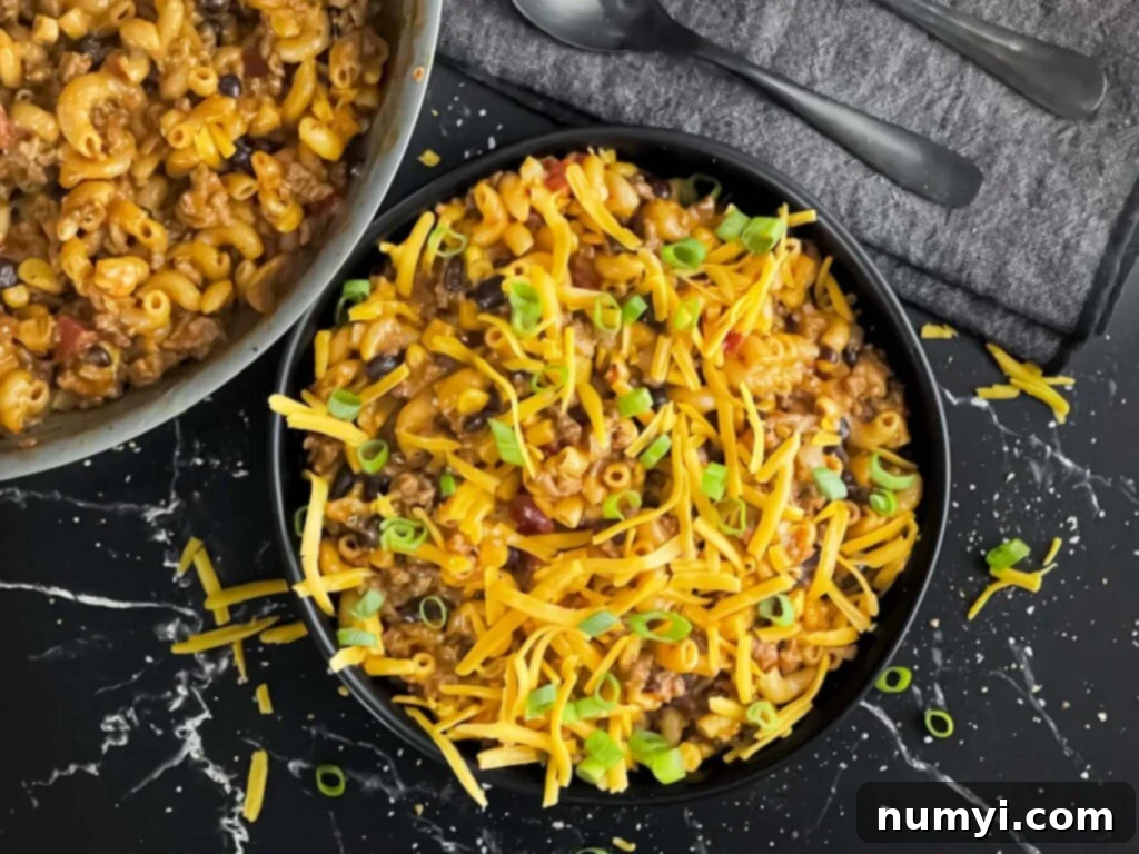 A vibrant and cheesy one-pot taco pasta skillet dinner served in a dark bowl, ready to eat.