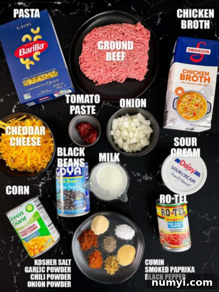 A collection of fresh ingredients laid out on a dark surface, including ground beef, spices, pasta, and vegetables, ready for a Taco pasta skillet.