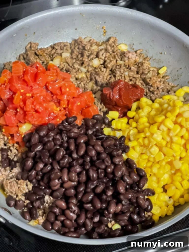 Fresh vegetables like corn and black beans added to seasoned ground beef in a skillet.