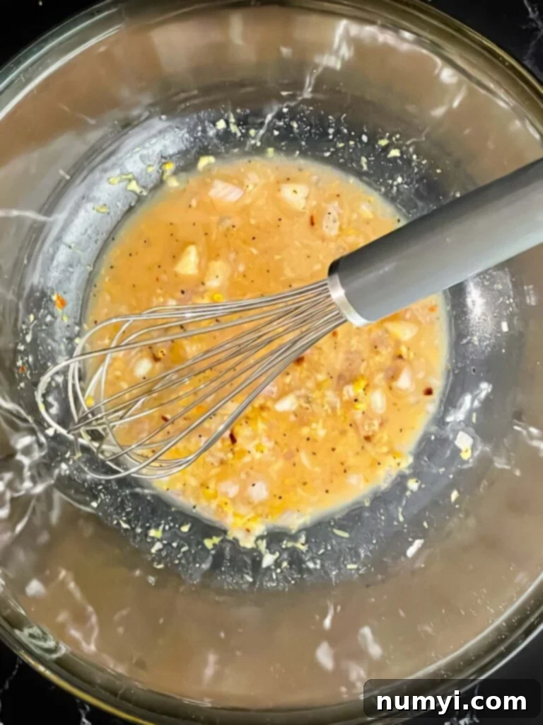 Minced shallots, garlic, and other dressing ingredients in a glass bowl, ready to be mixed.