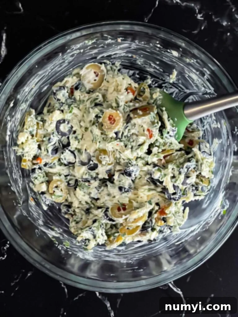 Olive cheese bread topping mixed together in a glass bowl, ready to be spread.