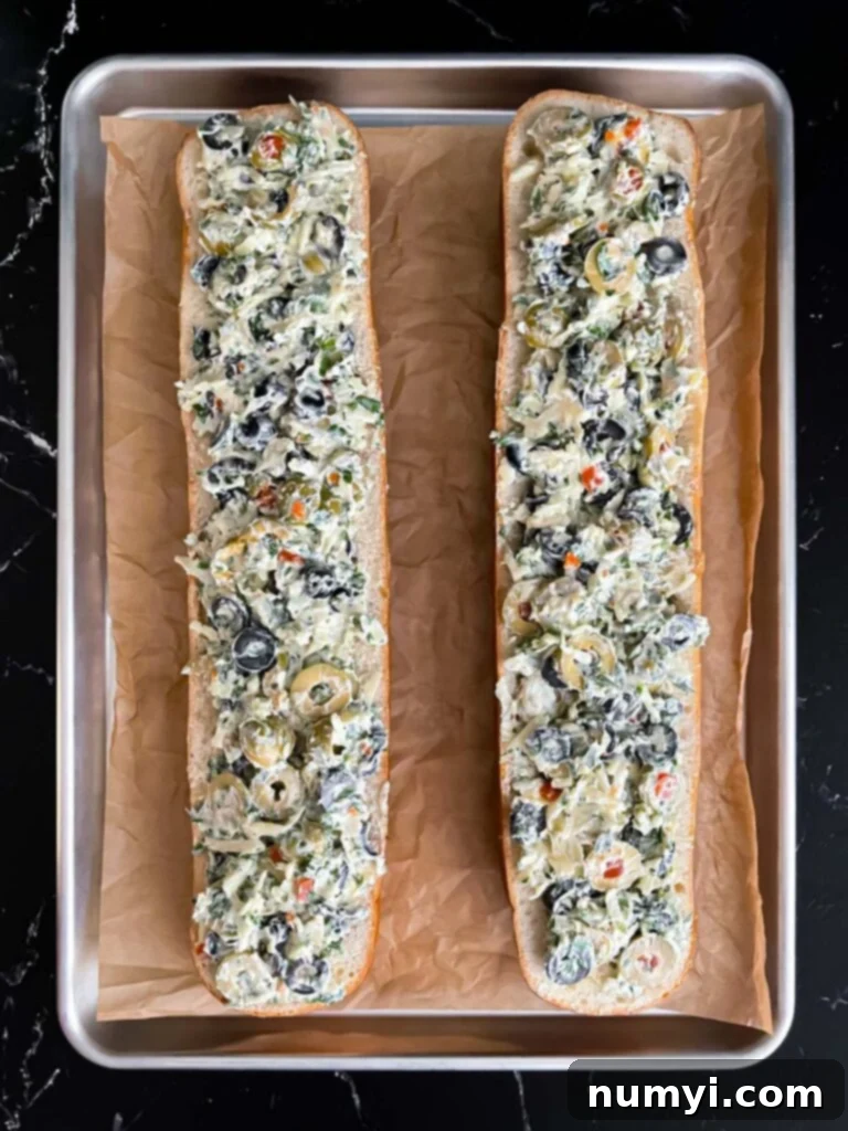 Unbaked olive cheese bread on a parchment paper lined baking sheet, topped with cheese.