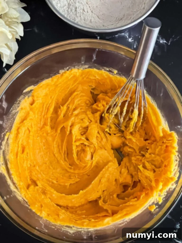 Pumpkin snickerdoodle wet ingredients, including pumpkin, egg, and vanilla, fully combined and whisked smooth in a clear glass bowl.