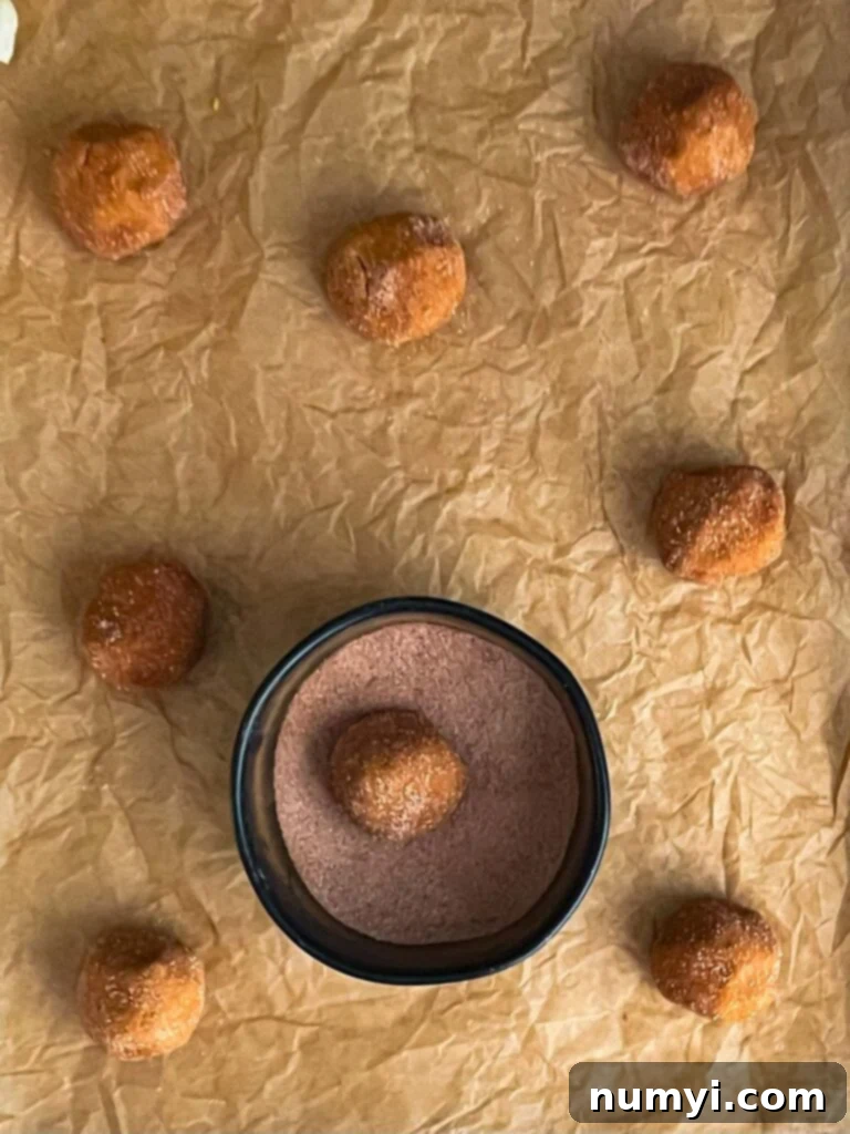 Uniform pumpkin snickerdoodle cookie dough balls, generously coated in cinnamon sugar, neatly arranged on a parchment paper lined cookie sheet.