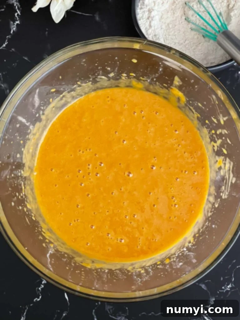 Wet ingredients for sweet potato bread recipe, including eggs and vanilla, mixed in a glass bowl.
