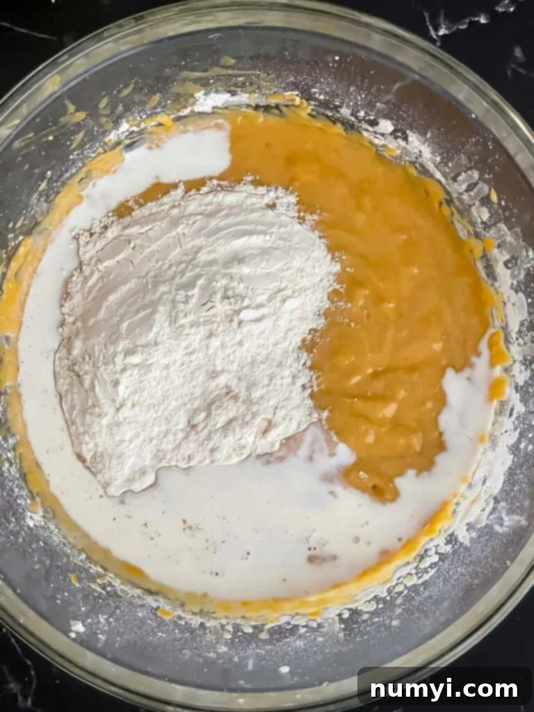 Dry ingredients and half and half being added to the sweet potato bread batter, showing streaks of flour remaining.