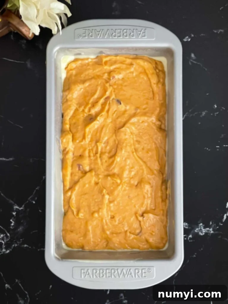 Sweet potato bread batter carefully poured into a greased loaf pan on a dark surface, ready for baking.