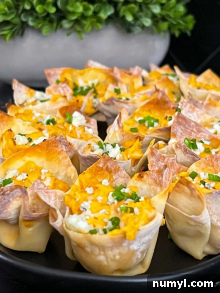 Buffalo chicken wontons garnished with chives and blue cheese crumbles on a cutting board.