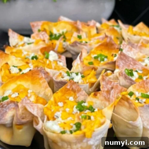 Buffalo chicken wontons garnished with chives and blue cheese crumbles on a cutting board.