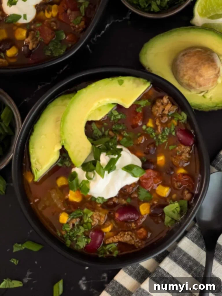 Bowls of taco soup in dark bowls with many garnishes including cilantro, sour cream, and tortilla chips.