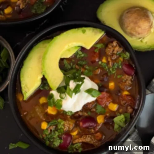 Bowls of taco soup in dark bowls with many garnishes.