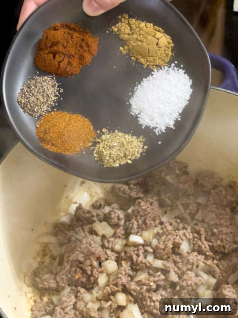Spices being sprinkled over cooked ground beef and onions.