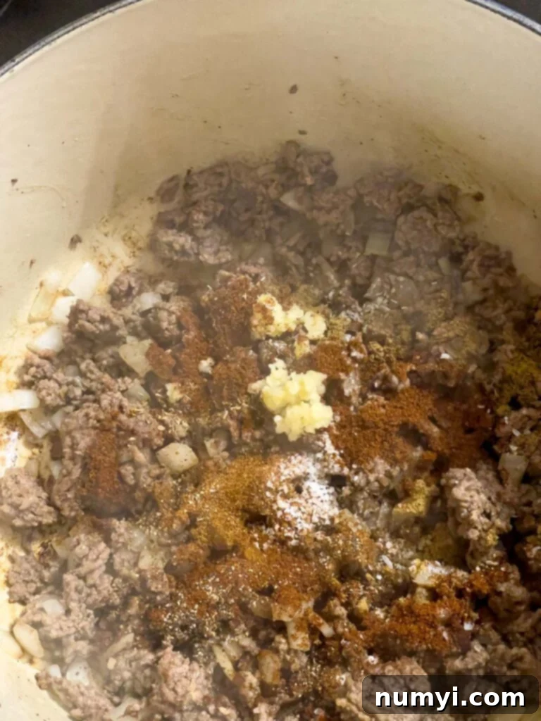 Spices mixed into cooked ground beef and onions in a dutch oven.