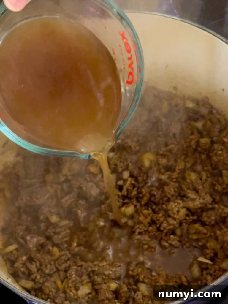 Beef broth being poured into the dutch oven with ground beef and spices.