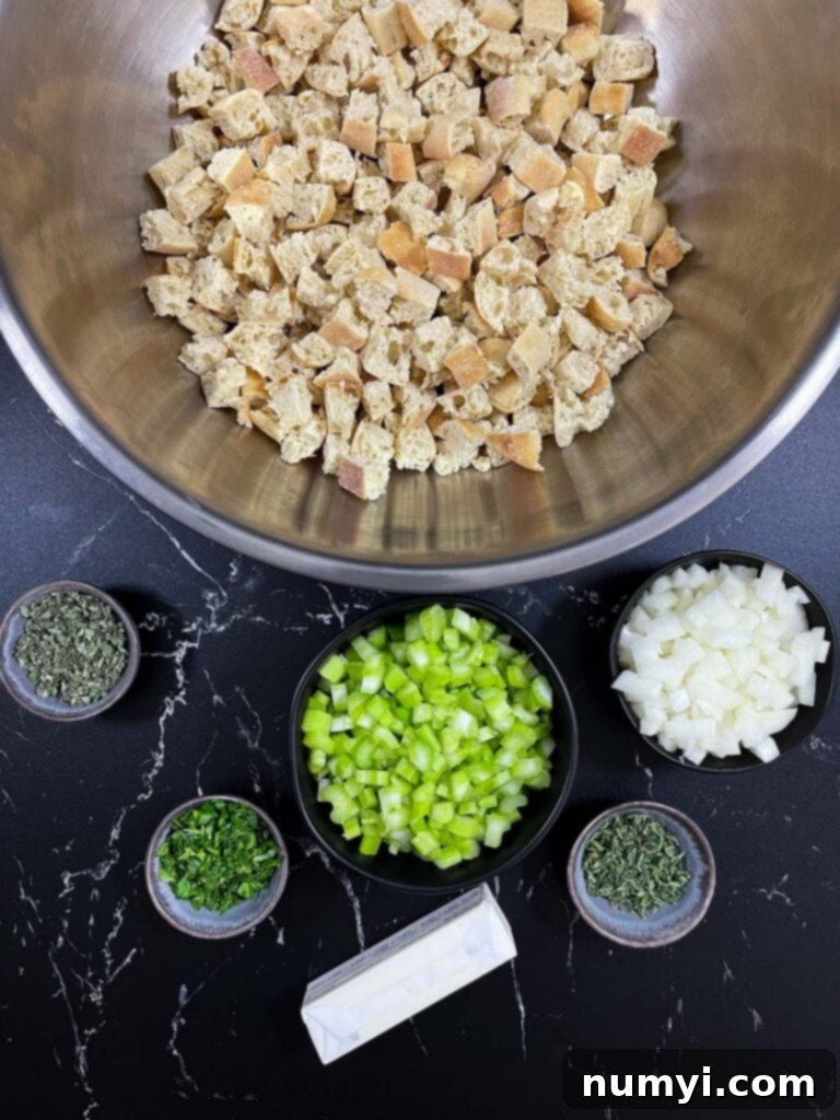 Dried bread cubes in a large mixing bowl, alongside prepared celery, onion, and fresh herbs, ready for the stuffing mixture.