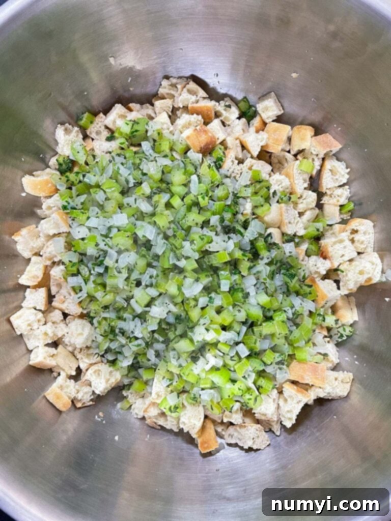 Cooked aromatic vegetables being added to the bowl of dried bread cubes, preparing for the final mix.